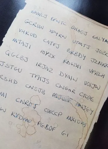 A page from a one-time pad — handwritten five-letter blocks of random letters on aged, stained paper