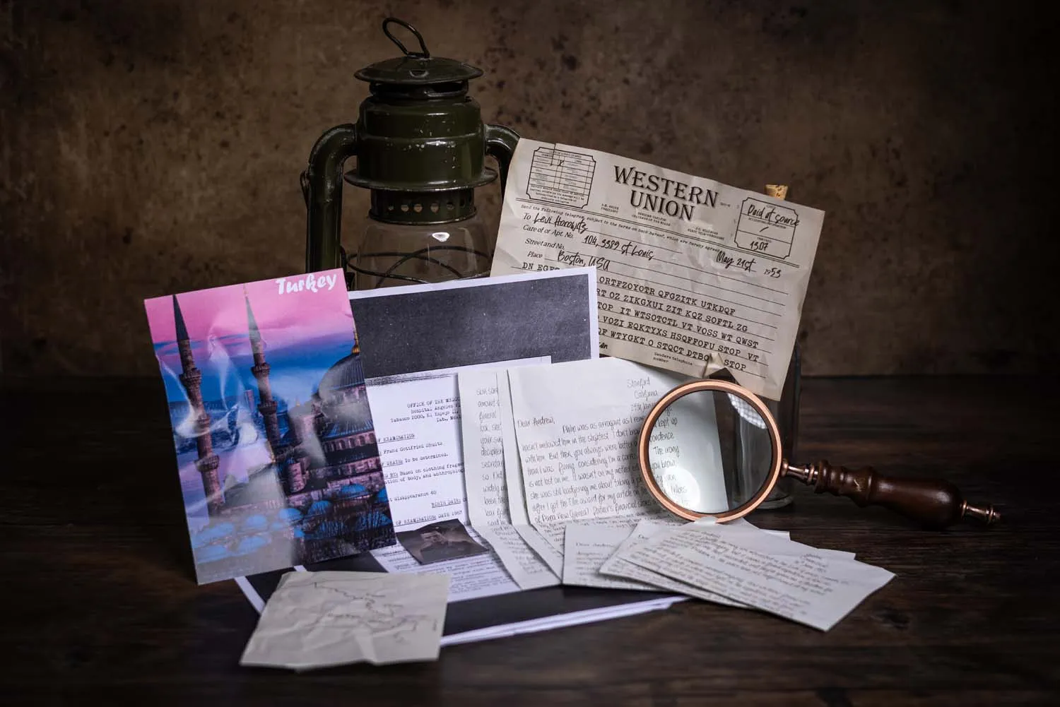 A wide shot of a Cosykiller case file spread across a dark wooden desk — magazine, hurricane lamp, photographs and ciphers